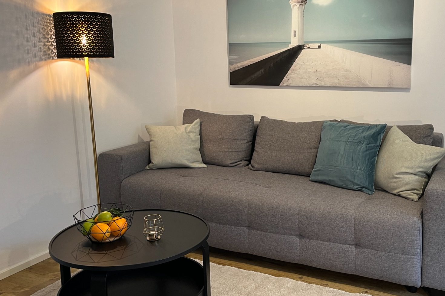 Homestaging_optimale_Präsentation_Ihres_Objektes dekoriertes Wohnzimmer mit Sofa, Kissen, Bild an der Wand, elegante Stehlampe und einem Couchtisch mit Obstkorb