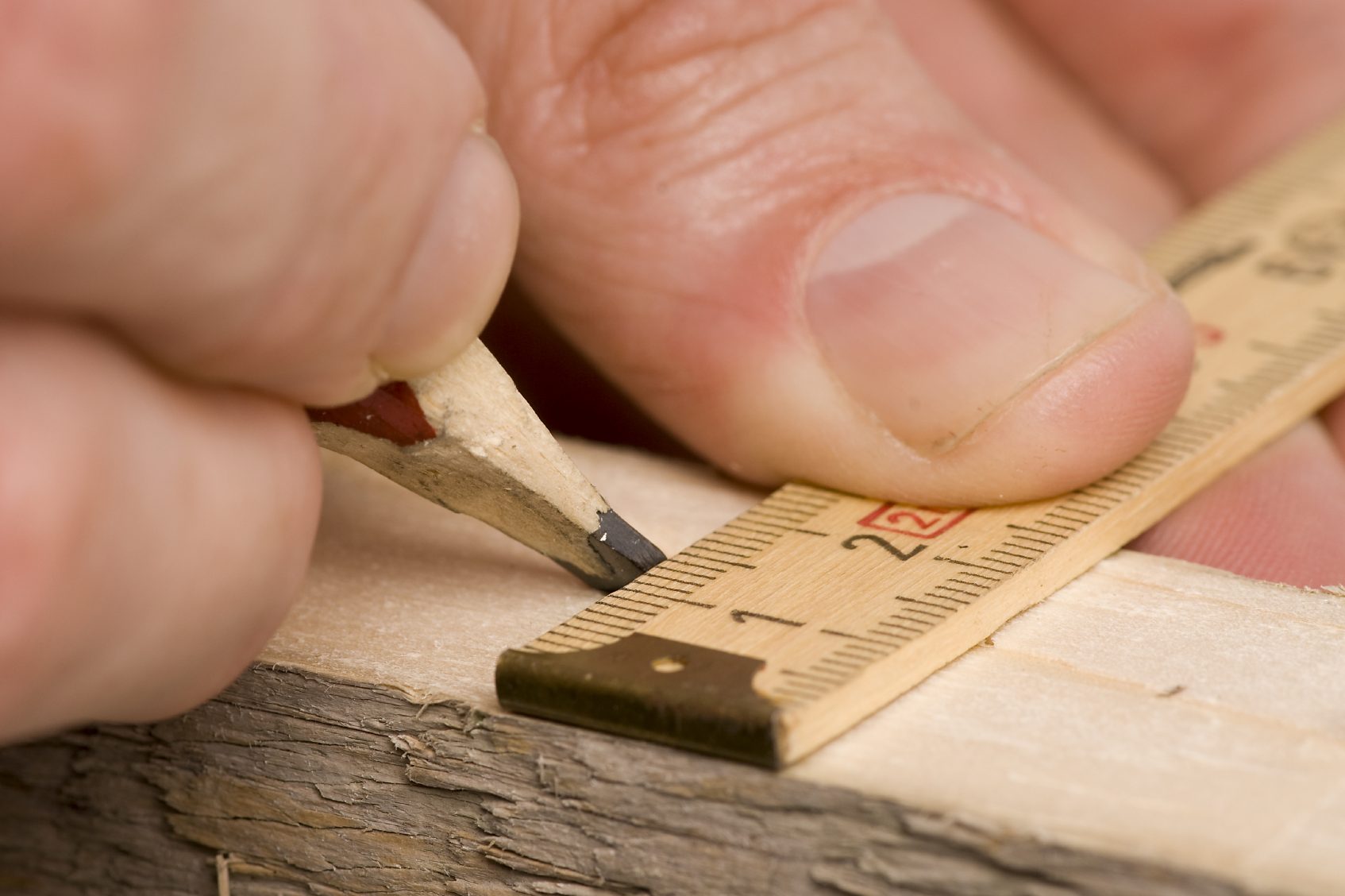 Maß_Lineal Eine Hand hält einen Bleistift und markiert eine Linie auf einem Holzstück mit einem Zollstock. Maßgetreu genau präzise Arbeiten