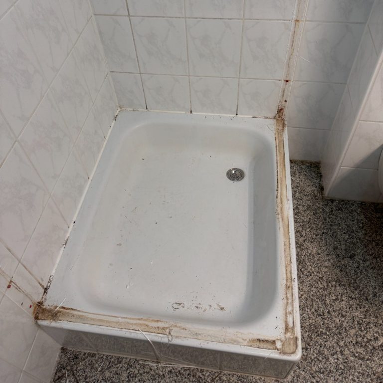 Bad_vorher Duschtasse ohne Wände mit sichtbaren Abnutzungsspuren und Schmutz entlang der Kanten.