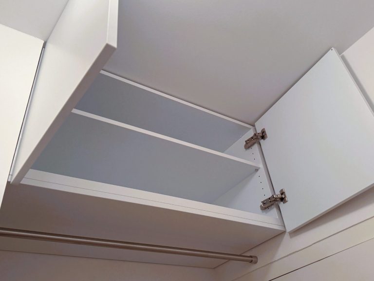 Oberschrank im Flur Weißer Deckenschrank mit zwei offenen Türen und zwei Regalen.