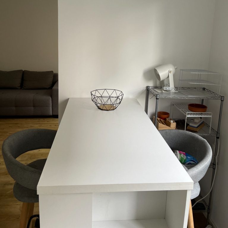 Essbereich_Küche_vorher Minimalistischer Essbereich, kale Wände, mit einem schmalen weißen Tisch und zwei grauen Hochstühlen.